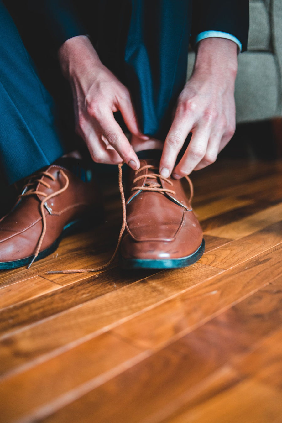Brown leather derby shoe being laced on a wooden floor